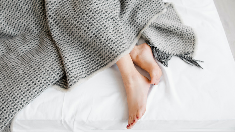 Female feet sticking out from under a blanket on a white linen bed