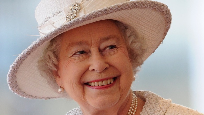 Queen Elizabeth smiling in a big hat and pearls