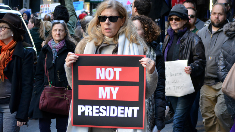 A well-dressed woman holding a "not my president" poster