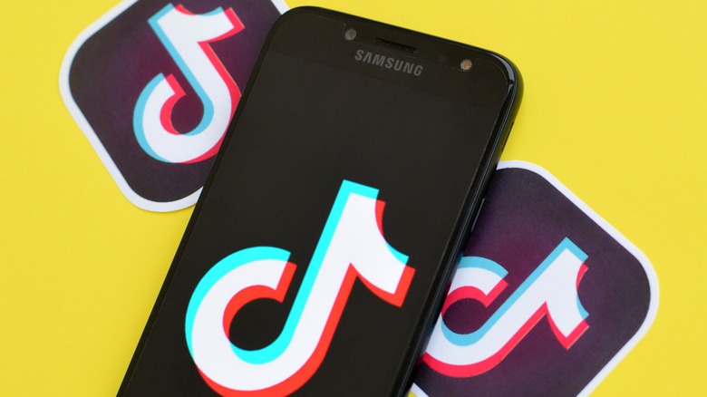 TikTok logos and phone with TikTok logo on a yellow background.