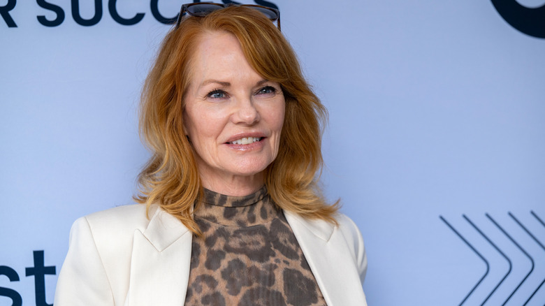 Marg Helgenberger smiling in front of a blue background wearing leopard print and white
