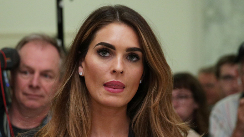 Hope Hicks wearing a black blazer and shirt while surrounded by reporters as she's leaving a hearing room.