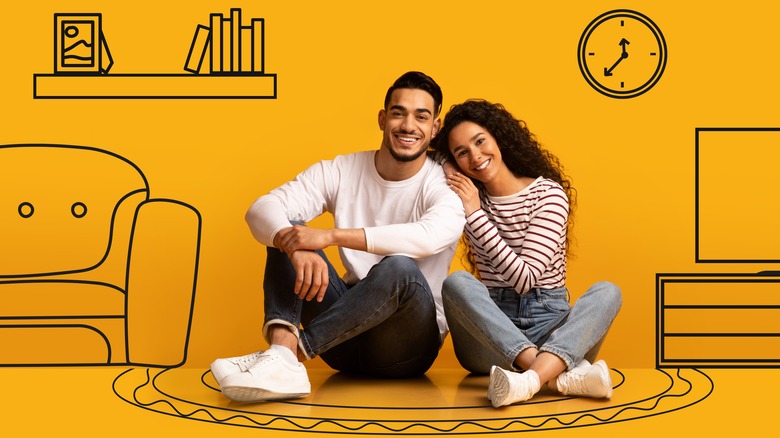 Young man and woman smiling on orange background with cartoon furniture