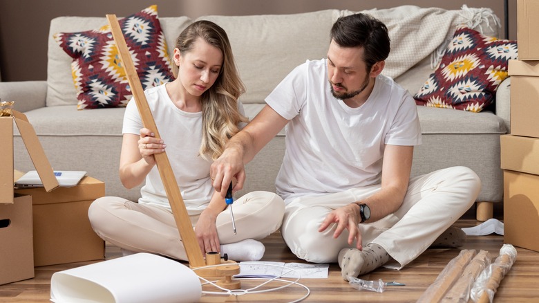 Man and woman assemble furniture in front of a couch