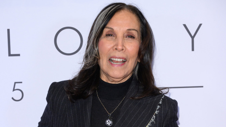 Olivia Harrison smiling while posing at an event in a black pinstriped jacket