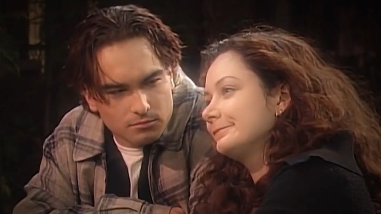 Sara Gilbert smiles and looks off into the distance as Johnny Galecki looks at her while filming an episode of "Roseanne."