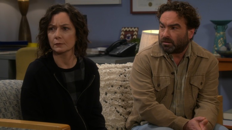 Sara Gilbert and Johnny Galecki frown on a couch while filming an episode of "The Conners."