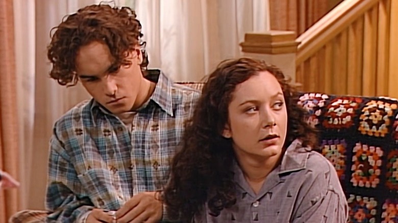 Johnny Galecki and Sara Gilbert look concerned as they sit together on the living room couch while filming "Roseanne."
