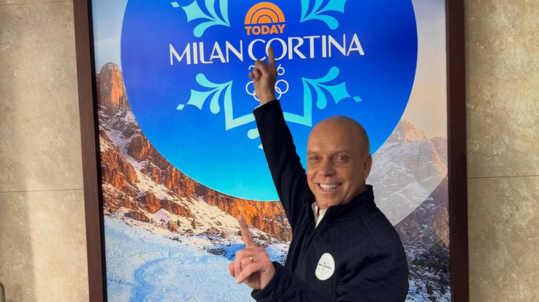 Scott Hamilton smiles and points to a 2026 Milan Olympics sign.