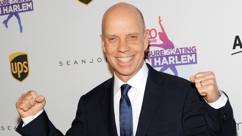 Former U.S. figure skater Scott Hamilton smiles on the red carpet with his fists in the air.