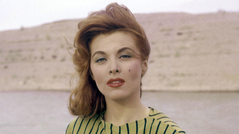 The actor who played Ginger in "Gilligan's Island" poses as a young woman outside wearing a striped  green shirt with her hair blowing in the wind