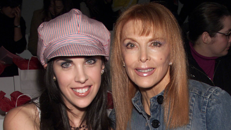 Actor Tina Louise sits at a fashion show smiling next to her adult daughter who wears a hat