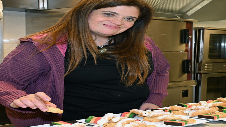 Alex Guarnaschelli smiles in an industrial kitchen wearing a purple jacket