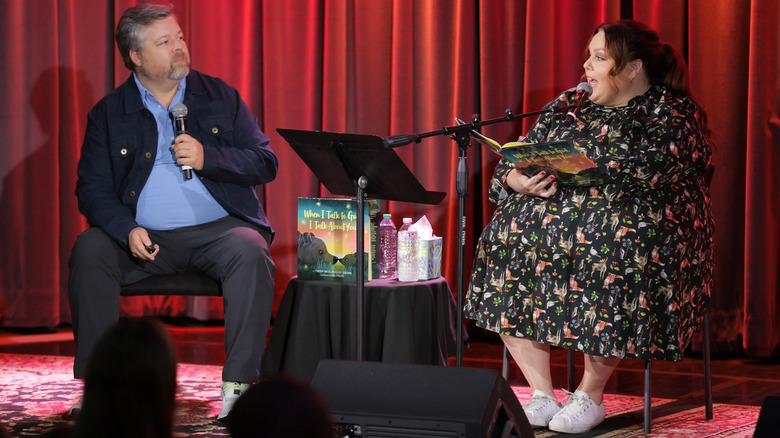 Chrissy Metz onstage with Bradley Collins reading one of her books to an audience.