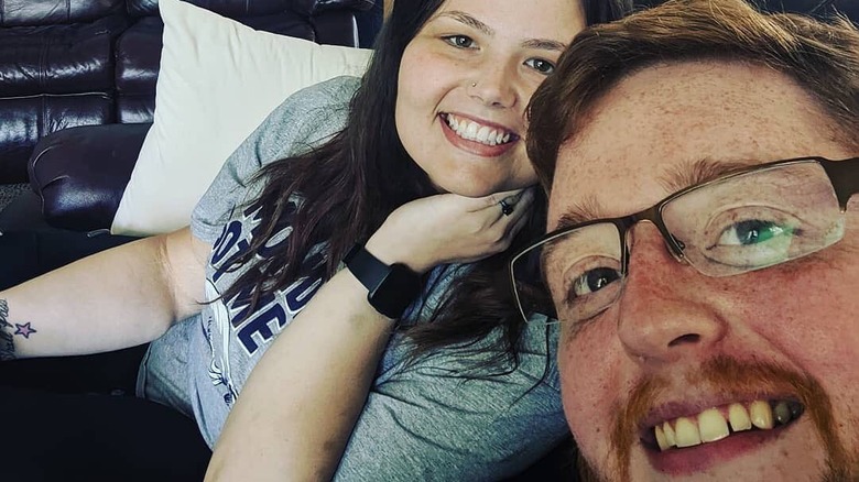 Justin McSwain and Christina Phillips smile in a selfie together on the couch.