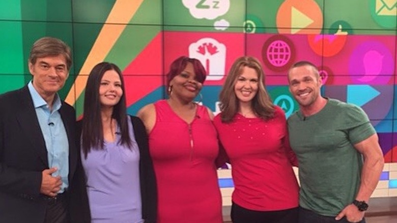 Christina Phillips poses with Dr. Oz and Chris Powell and two other women on a television set