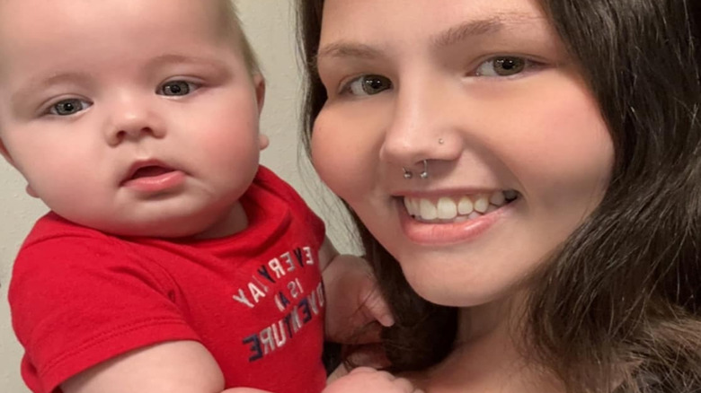 Christina Phillips smiles holding her baby in a red shirt