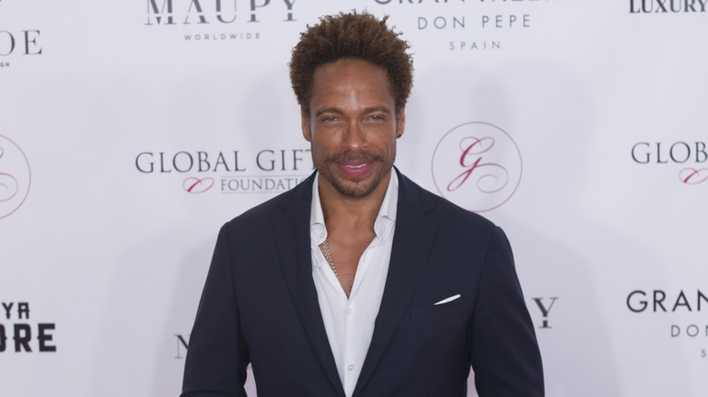 Gary Dourdan at a formal red carpet in a suit with a gold chain poking out from behind his white button down shirt