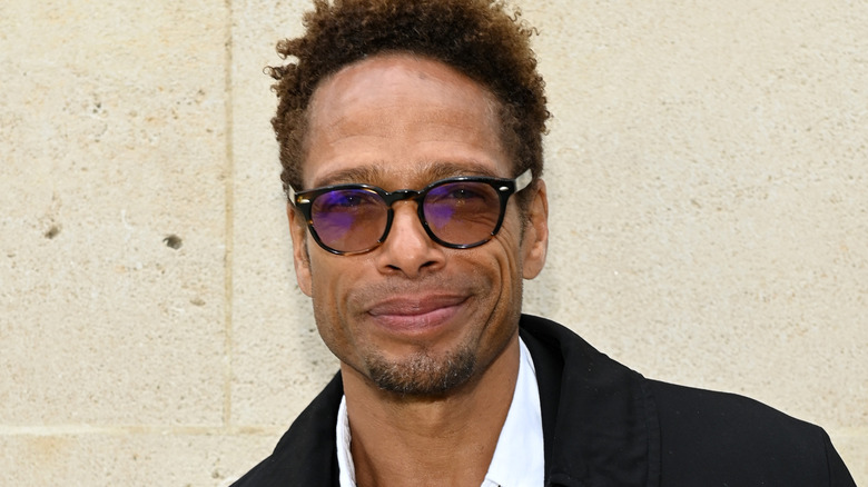 Gary Dourdan smiling for cameras in round frame sunglasses at an Hermes show in 2022