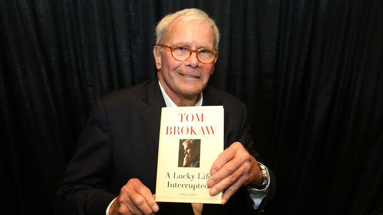 Tom Brokaw displaying copy of his book A Lucky Life Interrupted