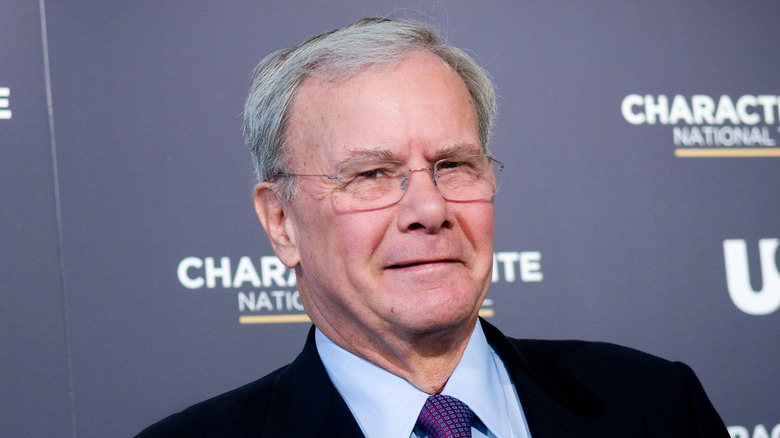 Tom Brokaw posing in front of a grey background