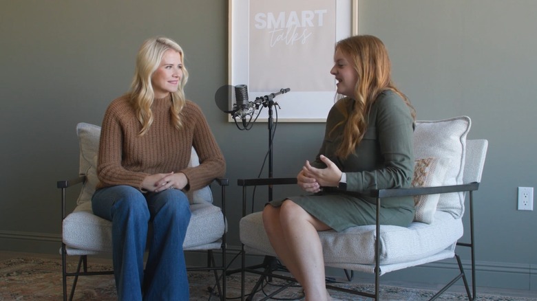 Elizabeth Smart and co-host Heather Stockdale speaking into a microphone in front of the Smart Talks logo