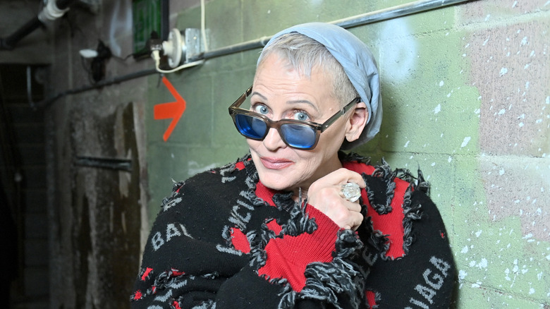 Lori Petty wearing sunglasses while posing in front of a concrete wall