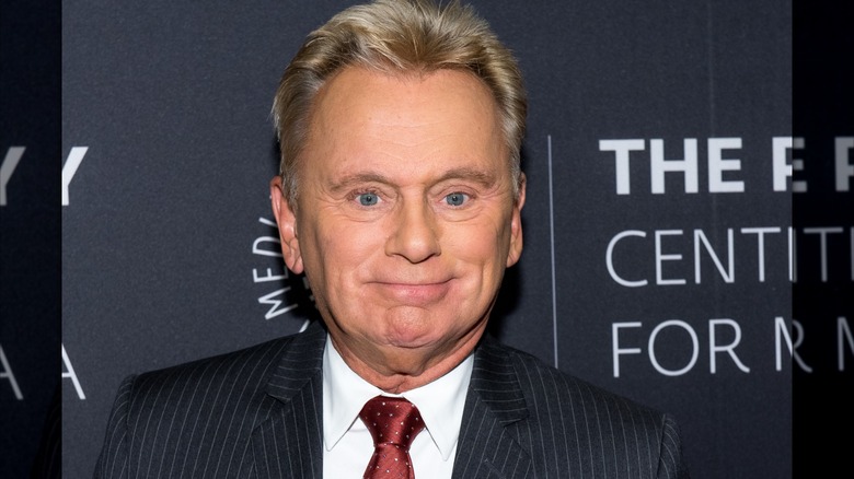 Pat Sajak smiling and posing at the Paley Center for Media wearing a black and white pin stripe suit.
