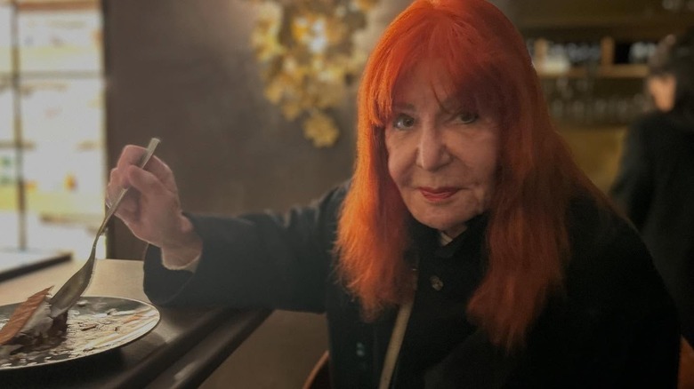 Sally Jessy Raphael with no glasses and orange hair, using a spoon to dig into dessert