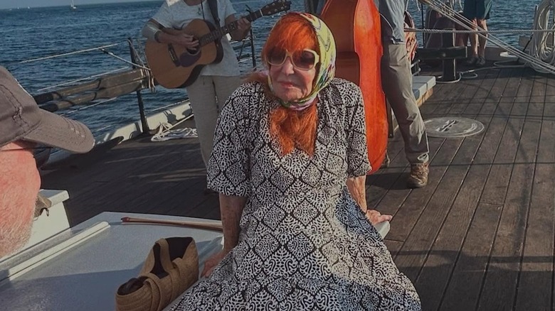 Sally Jessy Raphael with orange hair, big pink sunglasses, and a headscarf, sitting on a boat