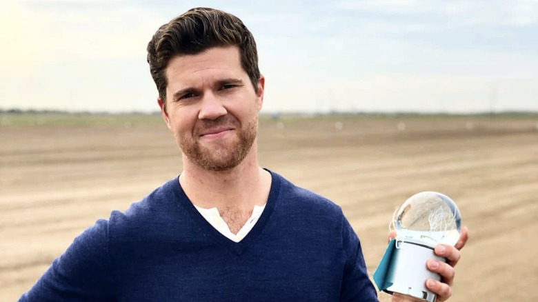 Actor Beau Wirick standing in a field wearing a blue sweater and holding a clear globe