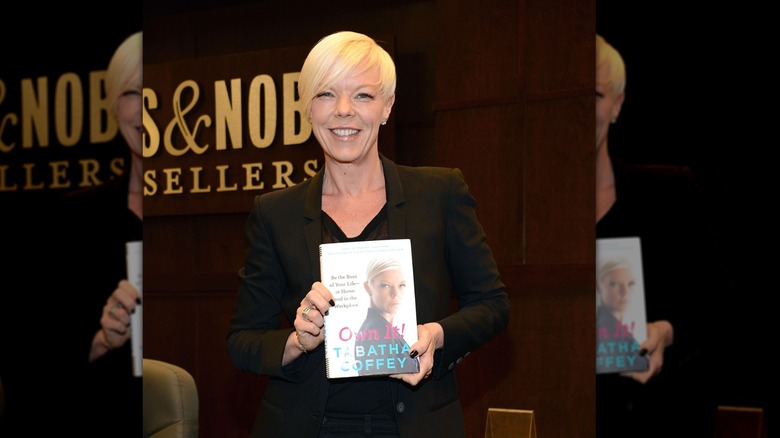 Tabatha Coffey holds up her book at Barnes and Noble wearing a black suit