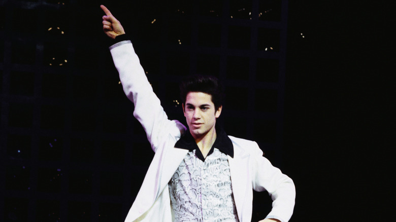 A young Adam Garcia in a white suit striking a disco dancing pose onstage