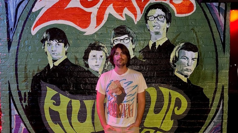 Robert Schwartzman posing with the poster of his Zombies documentary, "Hung Up on a Dream."