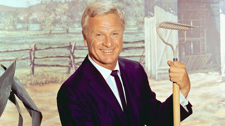 Eddie Albert smiling while holding a rake