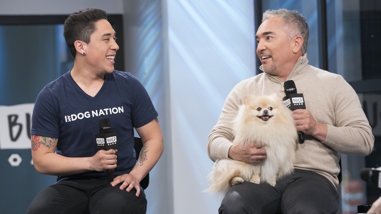 Cesar Millan holding a dog and a microphone, and his son Andre Millan in a Dog Nation shirt