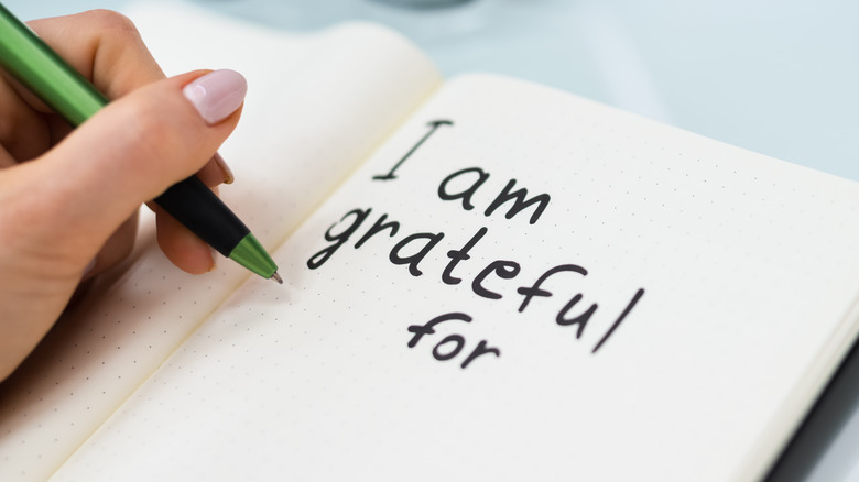 Woman writing "I am grateful for" in a journal