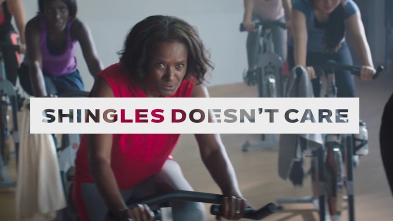 Woman taking a spin class with the phrase "Shingles Doesn't Care" across the screen