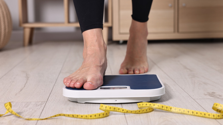 Woman stepping on floor scale with measuring tap next to it