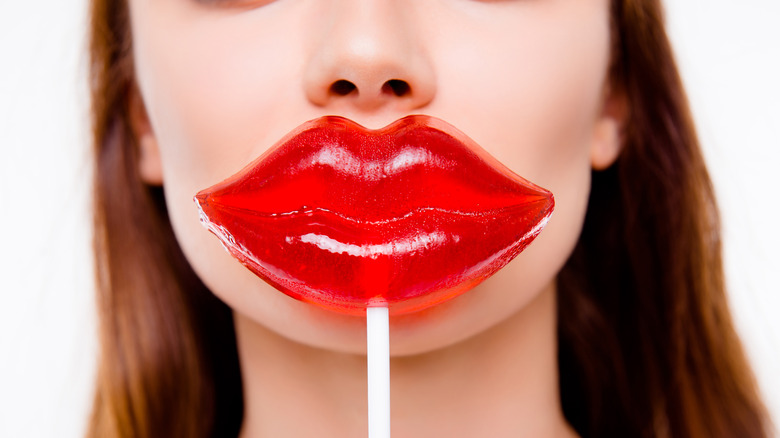 Woman holding a red lip-shaped sucker in front of her mouth.