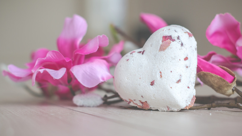 A heart shaped bath bomb near pink flowers