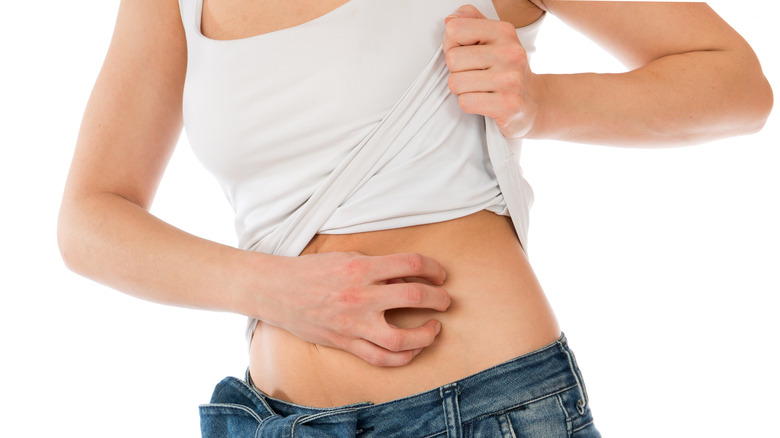 Woman lifting her white shirt to scratch her stomach