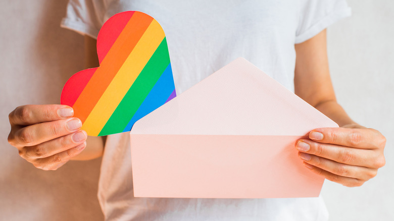 Hands pulling rainbow heart from envelope