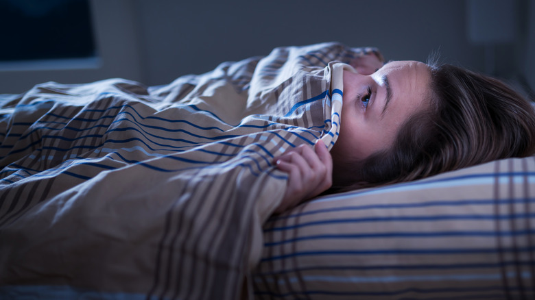 Scared woman under blanket in bed