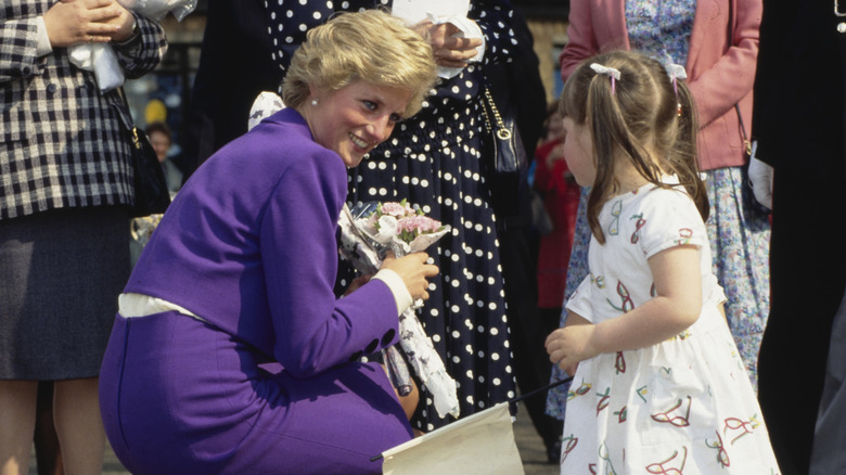 Princess Diana in a purple outfit smiling at a little girl