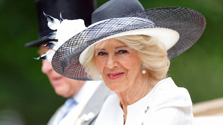 Queen Camilla in a white outfit and wide gray hat