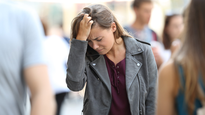 Woman holding her head in the middle of a crowd