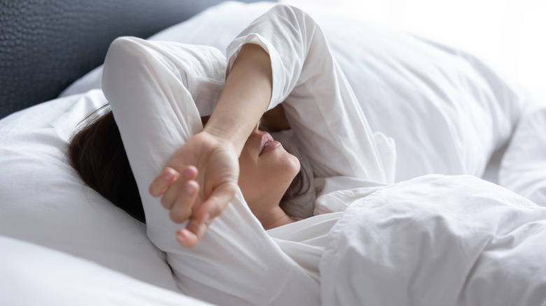 Woman laying in bed covering her face