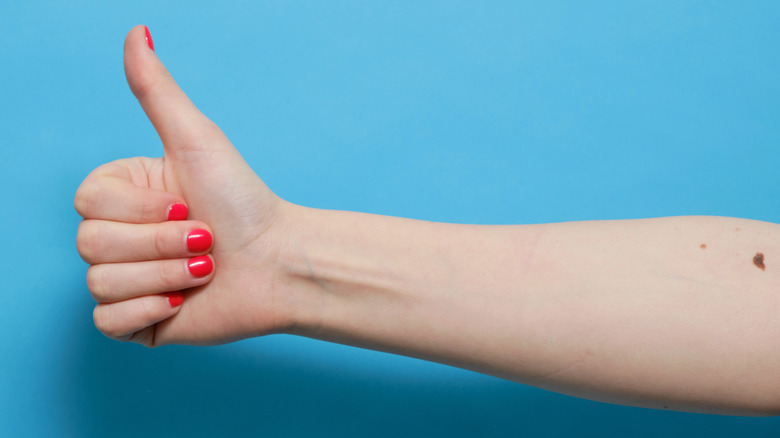 Person in red nail polish giving a thumbs up with a mole on their arm