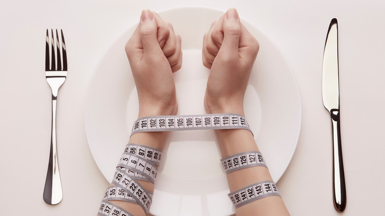 Wrists bound by measuring tape on a dinner plate